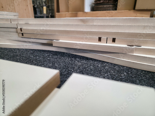 Stack of wood sheets arranged neatly in a workshop setting with tools in the background and natural light