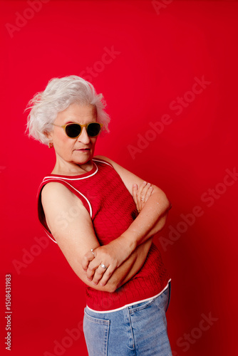 Woman in sunglasses and red top posing confidently against a red background
