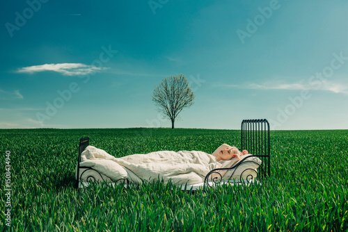Woman dreaming in a bed outdoors under a blue sky with a lonely tree in a green field