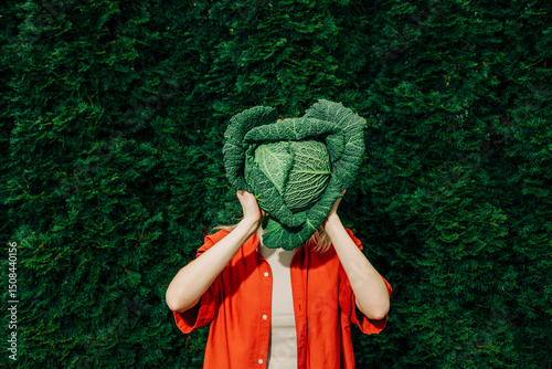 Woman in red shirt holding Italian kale in front of face outdoors