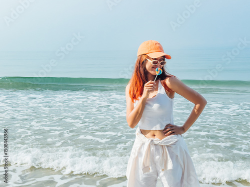 Young woman with colorful lollipop and orange hat enjoy the beach.