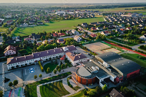 Fototapeta Naklejka Na Ścianę i Meble -  Aerial view of large school complex with classrooms, gymnasium, sports courts, surrounding suburban housing and green fields in small town