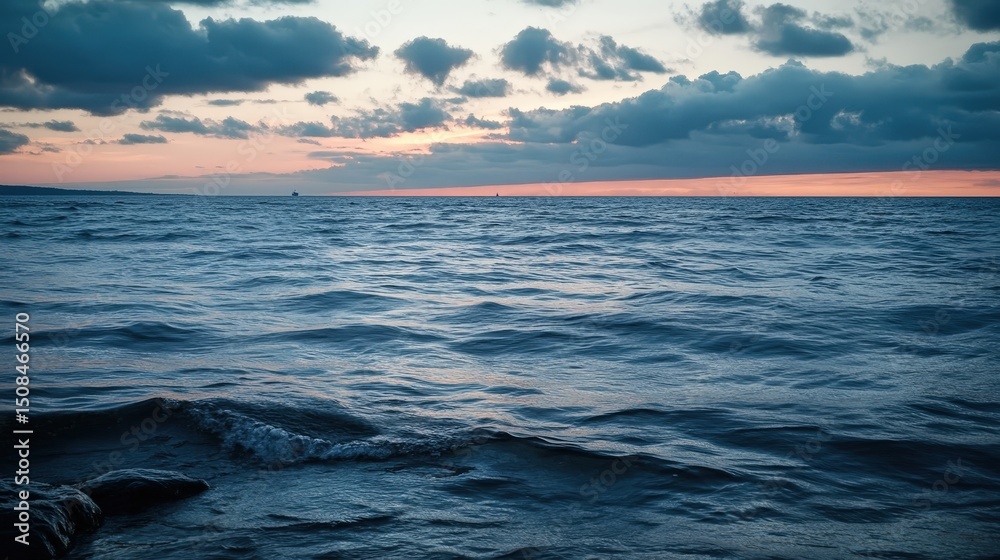 Obraz premium A tranquil ocean view at sunset with rippling waves and cloudy skies. Soft colors blend in the horizon, creating a calming atmosphere.