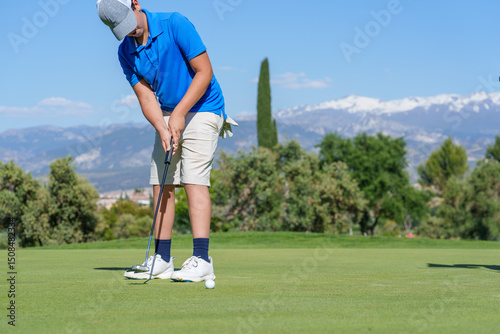 Young golfer putting the ball on a beautiful golf course with mountain views