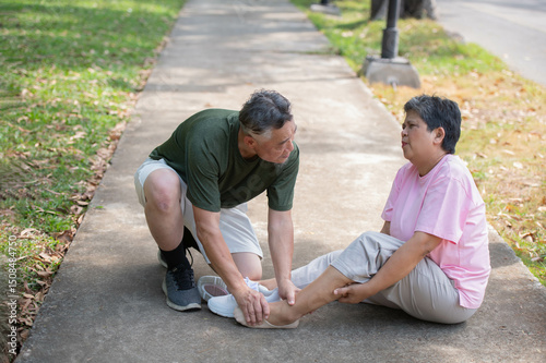 Elderly man gives first aid to wife who injured her ankle while exercising in a park photo