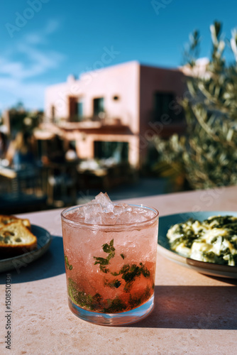 Refreshing pink cocktail with herbs on outdoor table during sunny brunch