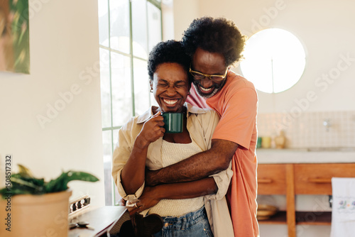 Mature man making his wife laugh in a tight hug at home