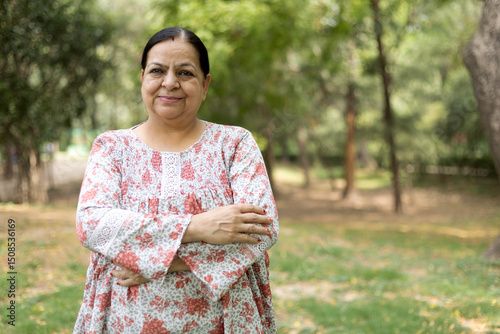 Indian elder woman arm crossed and looking at camera at park. Attractive, blonde, lovely, elegant and beautiful senior woman spending leisure time copy space