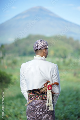 Temanggung, Central Java, Indonesia - Wednesday, July 27, 2022, 11.30 AM: Serene Mountain View Man in Traditional Attire Contemplates Nature's Majesty photo