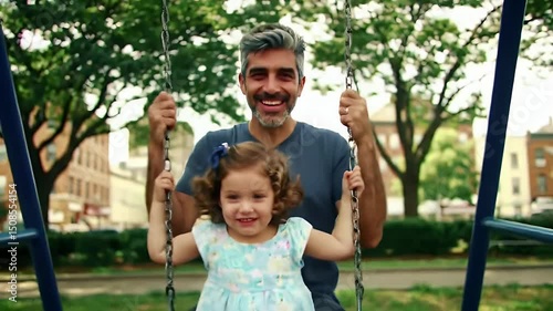 Father and daughter swinging in a city park on a sunny day