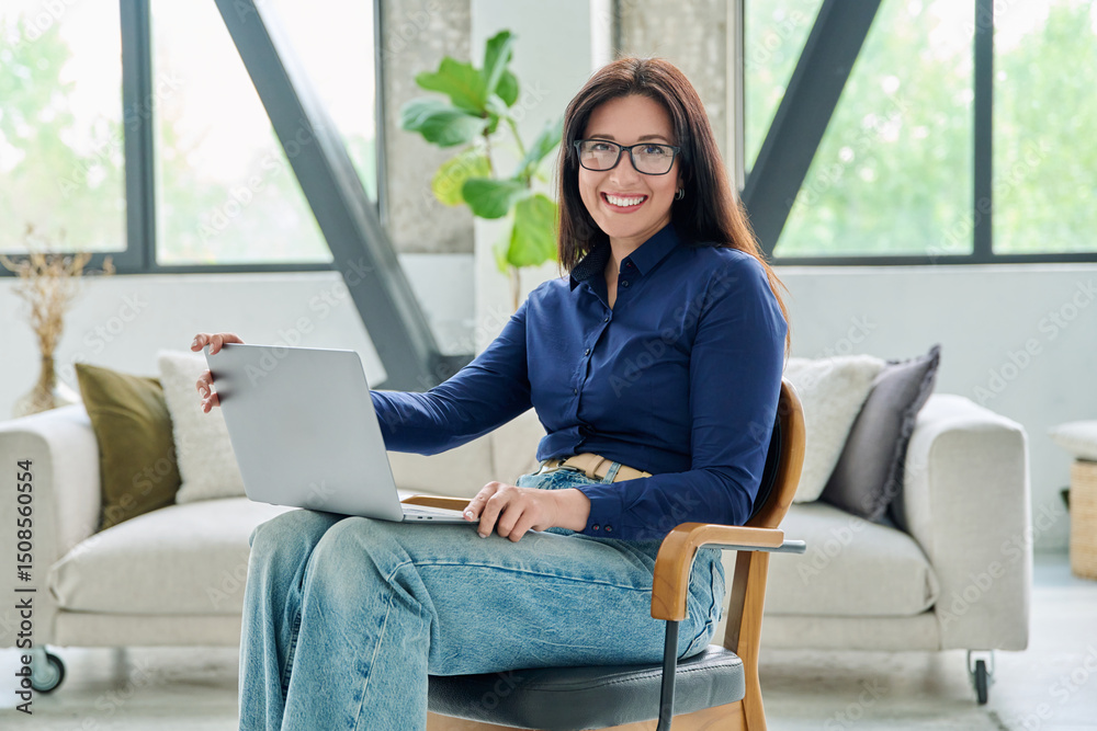 Portrait of smiling business woman with laptop in office with couch Portrait of smiling business woman with laptop in office with couch