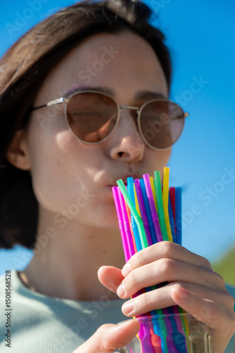 A girl drinks a summer drink from cocktail straws. Lots of colorful straws.