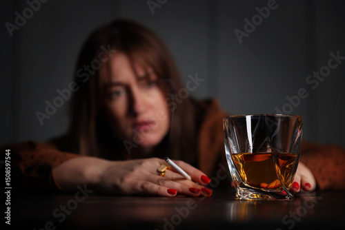 Alcohol addiction. Woman with glass of whiskey and cigarette at table indoors, selective focus photo