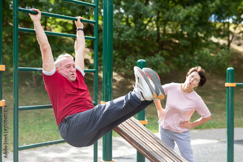 Canvastavla Elderly man and woman doing exercises on horizontal bars at outdoor sports groun