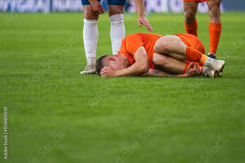 The injured footballer lies on the pitch and the opponent apologizes for the foul.