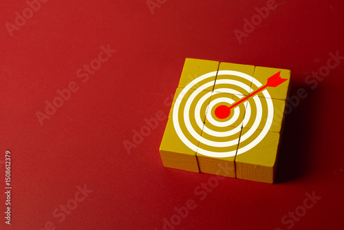 Concept of achieving goals,goal setting,business success, precision,marketing objectives and strategic targeting.,Red arrow hitting the center of a white target on wooden blocks over red background.