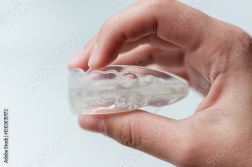 Person holding orthodontic silicone mouth guard for straightening or whitening children's teeth. Side view, close-up, on white background