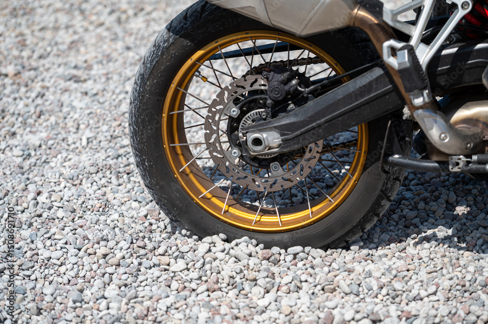 Obraz premium Close-up view of motorcycle wheel on gravel surface during sunny outdoor setting