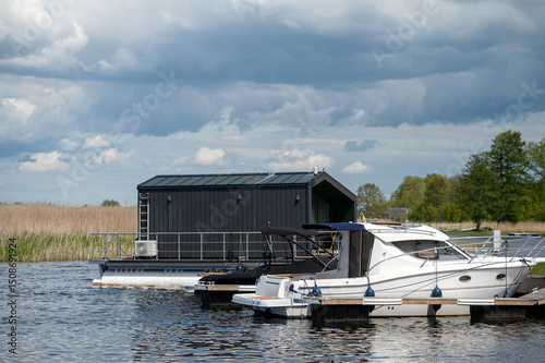 Houseboat moored next to yachts on a peaceful lake surrounded by greenery