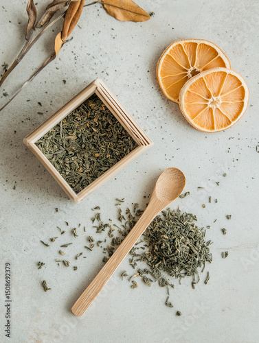 Flat lay of open eco tea box with loose-leaf herbal tea spilling on terrazzo counter, bamboo teaspoon, dried citrus slices, even diffused light, natural palette with soft greens and muted orange
