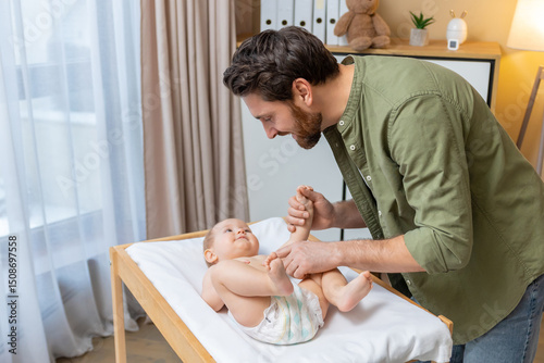 Dad changing a diaper to his little baby boy while the kid smiling and looking happy