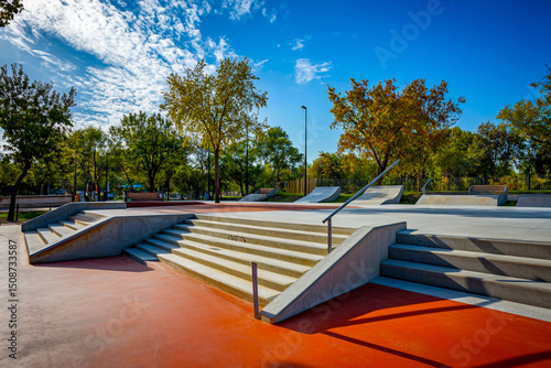 Concrete skatepark with stairs and handrails, surrounded by plants in the background, perfect for street skating and tricks.