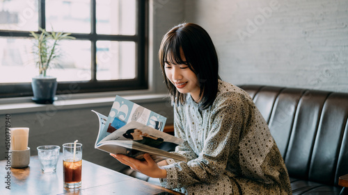 カフェのソファに座って雑誌を読む若い女性