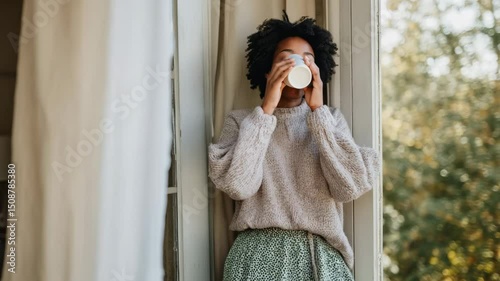 Serene woman drinking coffee on sunlit balcony, overlooking golden autumn landscape with soft morning light filtering through tree branches. Peaceful young woman relaxing, sipping warm beverage