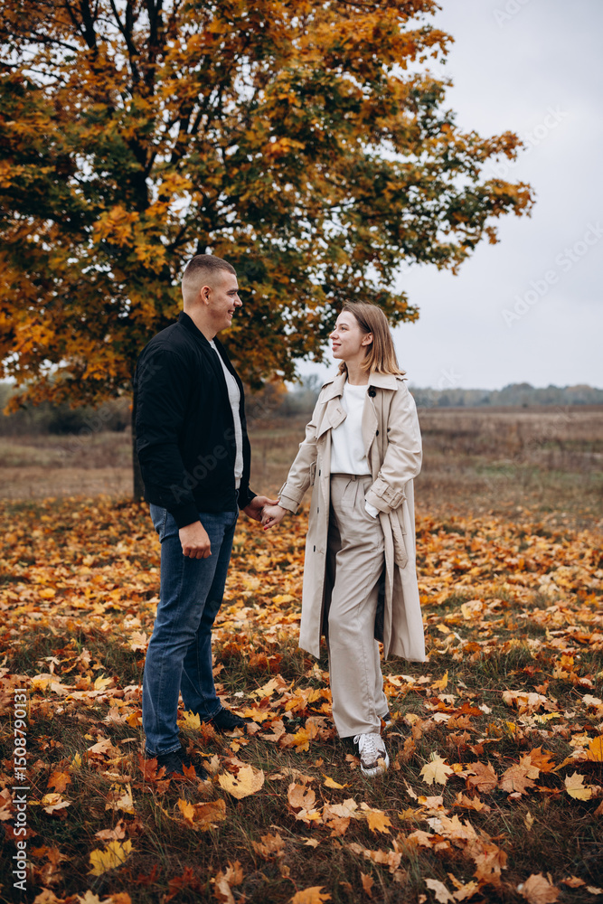 Fototapeta premium A couple hugging under a yellow-leaved autumn tree. Romantic walk in the fall park, warm atmosphere, love, and harmony surrounded by colorful foliage.