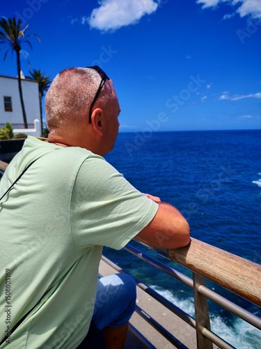 Adult male contemplating the sea view leaning on a railing, on a beautiful sunny day.view of a man in profile observing the Panorama.Handsome male tourist observing the sea, thinking.Enjoying the open