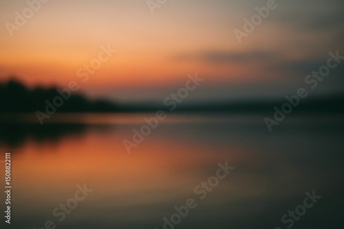 Defocused view of a lake at dusk with a soft glowing sunset reflecting on calm, still water..