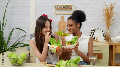 Black and white teenage friends working together to make a vegetable salad in the kitchen. Healthy food.