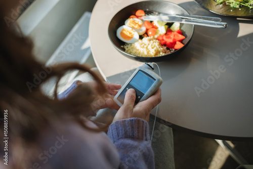 Overhead view of a woman sitting at a table injecting insulin with an insulin pump before a meal photo