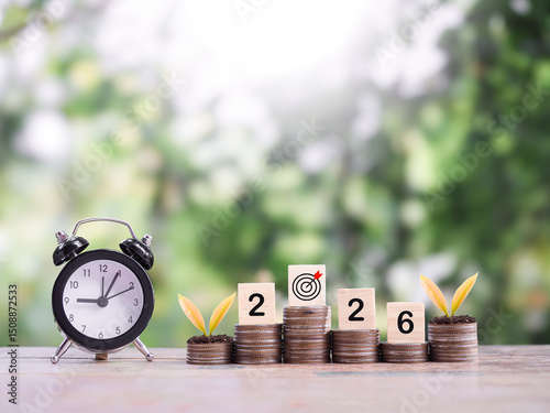 Black alarm clock, Wooden blocks with the number 2026 and plants growing up on stack of coins. The concept of saving money for manage time to success business in year 2026