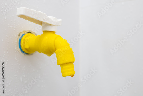 Yellow plastic faucet mounted on the wall in the bathroom
