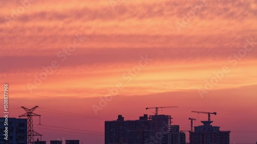 4k time lapse footage of moving beautiful sunset clouds and cranes working on city buildings top, orange clouds like fire on sky.