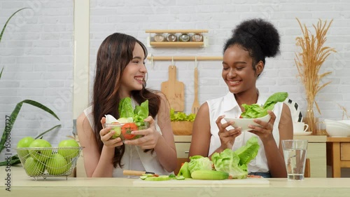 Black and white teenage friends working together to make a vegetable salad in the kitchen. Healthy food.