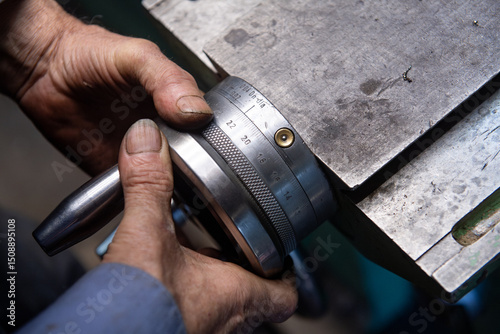 Close-up of rough, dirty hands skillfully adjusting the manual feed device on a lathe. The focus is on the hands and the intricate details of the mechanism, highlighting the craftsmanship in the machi