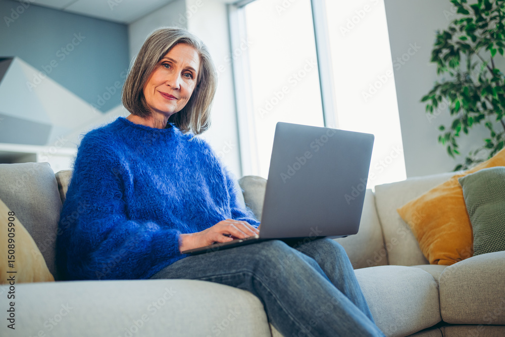 Mature woman enjoying leisure time on a sofa with a laptop, showcasing modern lifestyle, comfort, and casual elegance. Mature woman enjoying leisure time on a sofa with a laptop, showcasing modern lifestyle, comfort, and casual elegance.