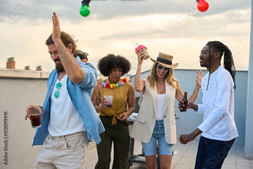 Friends dancing and drinking at rooftop party during sunset
