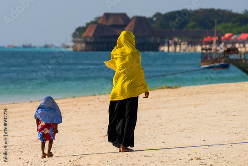 Rear view of woman and child with headscarf looking at the sea during the sunny day, Zanzibar, tanzania