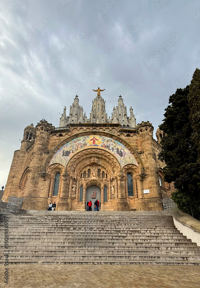 Obraz premium Temple of the Sacred Heart. Tibidabo. Majestic stone church with intricate facade and towering spires, surrounded by lush greenery and steps leading to the entrance, showcasing architectural beauty