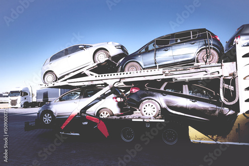 Passenger cars on a car hauler trailer in a parking lot.