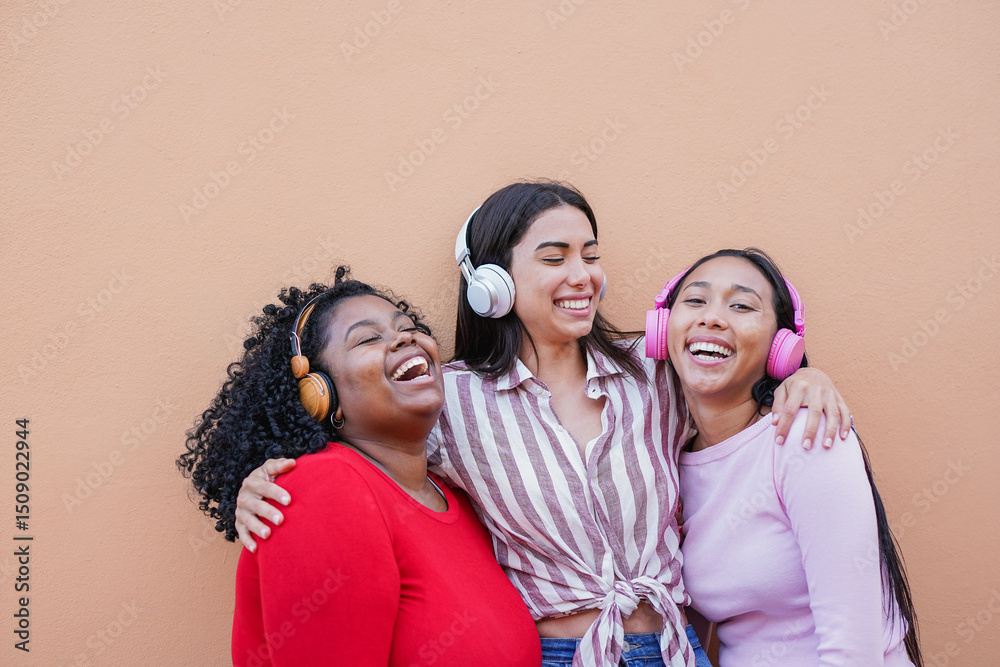 Obraz premium Happy multiracial women having fun listening music playlist with wireless headphones in the city - Generation z, urban lifestyle and young people concept