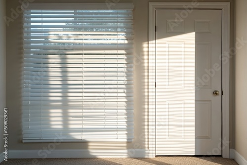 Sunlight streaming through white blinds casts soft shadows on beige wall and door. Clean, minimal interior. Morning light. Calm atmosphere. Peaceful home scene. Space for text. Warm tones