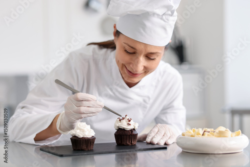 Tableau sur toile Confectioner decorating cupcake with pieces of chocolate in kitchen