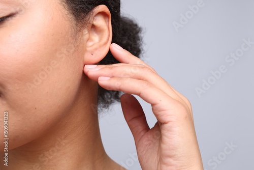 Young woman with pierced ear on light grey background, closeup photo