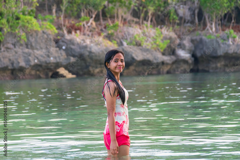 Fototapeta premium Young asian woman in swimsuit standing in tropical river with rocks behind