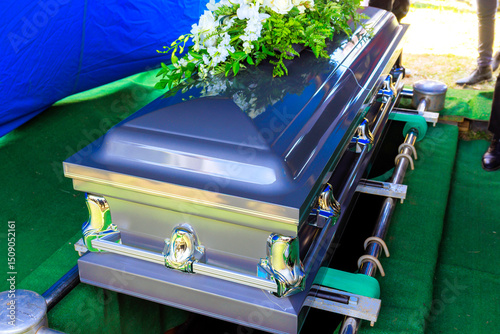 Funeral silver casket as decorated coffin is lowered at during burial ceremony.
