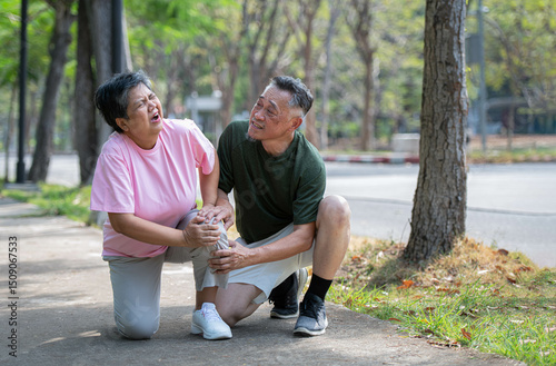 A middle-aged woman cries in pain as she walks in a park with her husband providing first aid at her side.